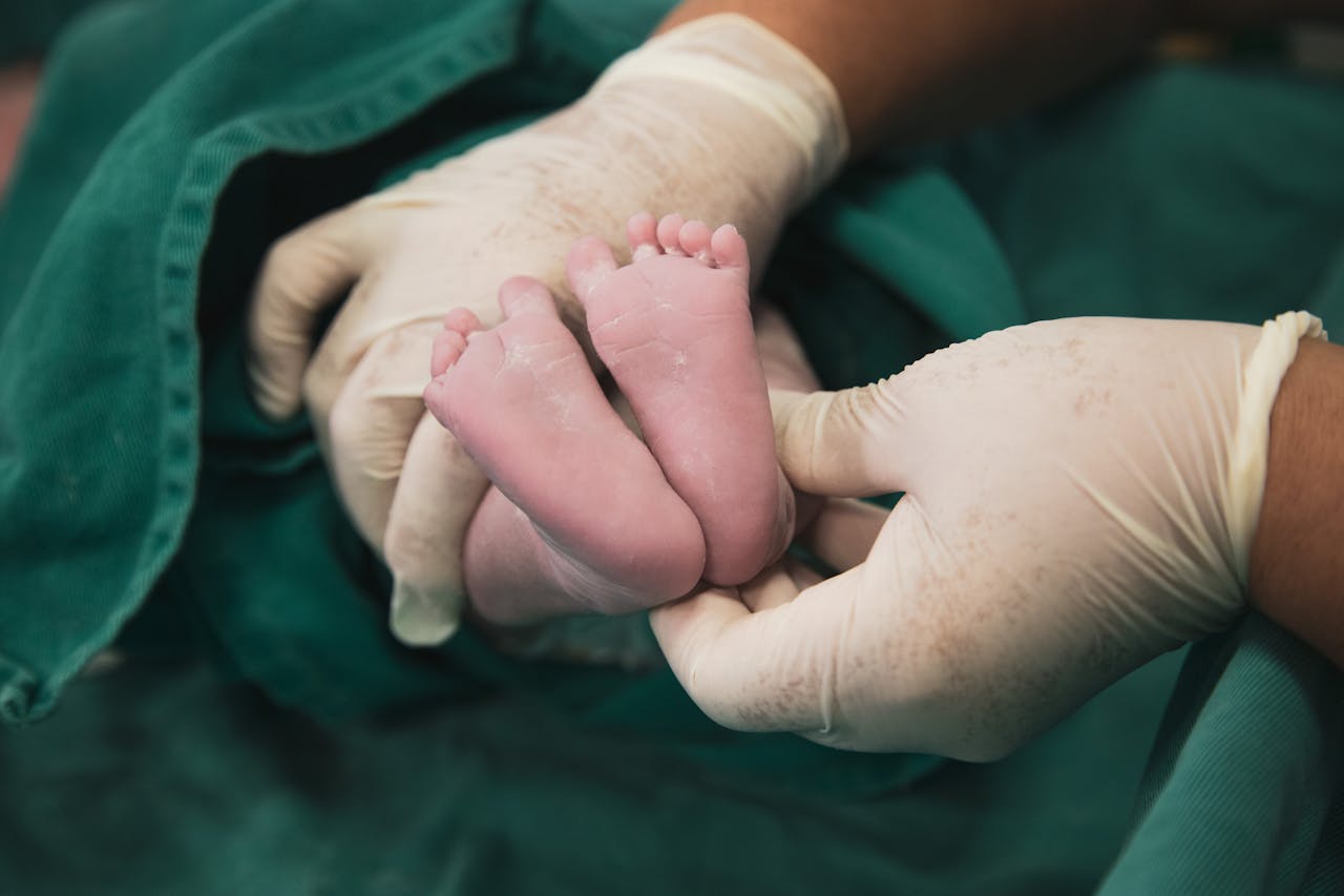 A newborn's feet being gently held by a nurse in latex gloves in a hospital environment.